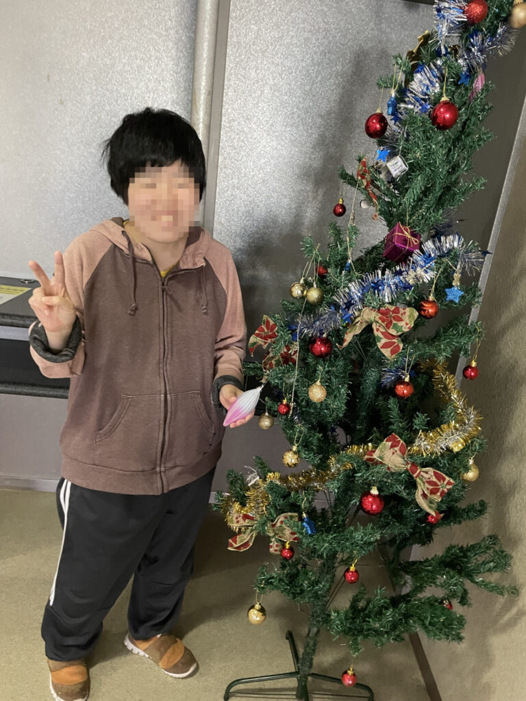 クリスマスツリーの前でピースをする人